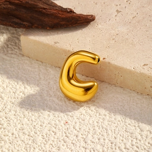 Polished gold-plated C-shaped earring on a minimalist stone and wood texture background