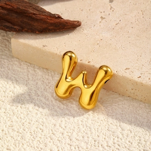 Polished gold W letter pendant in liquid metal style on a textured stone surface