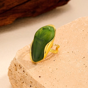 Anello con pietra verde irregolare e fascia dorata ondulata su sfondo in pietra naturale