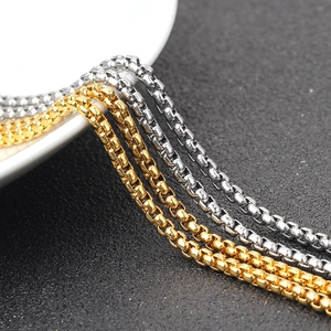 Dettaglio di catene box in oro e argento lucido su superficie scura materica