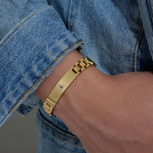 Dettaglio del bracciale massonico in acciaio dorato su uno sfondo di giacca di jeans
