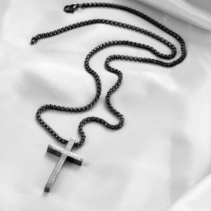 Macro detail of black stainless steel cross pendant featuring engraved religious scripture