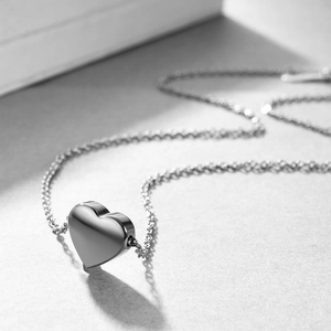 Detalle del collar con colgante de corazón plateado pulido con sombra y textura metálica