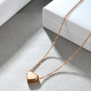 Detalle de un collar con colgante de corazón en oro rosa sobre fondo gris con textura