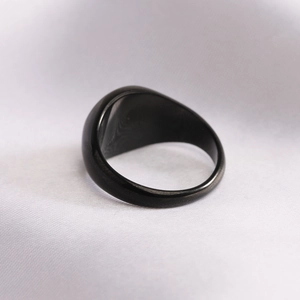 Macro shot of matte black signet ring on white silk background showcasing minimal design