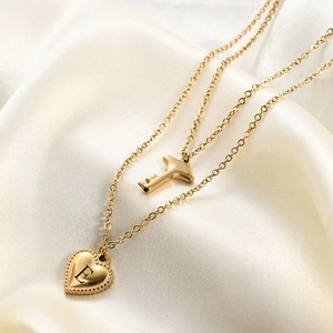 Dettaglio della collana dorata a due strati con ciondolo a chiave e cuore inciso E