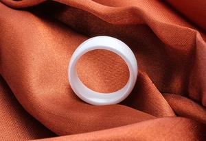Macro shot of minimalist white ceramic ring on smooth orange silk fabric background