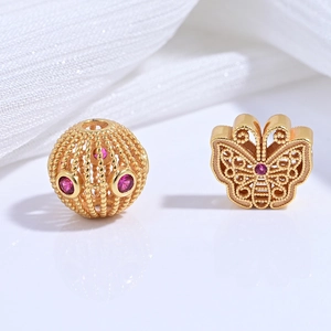 Macro detail of gold-plated hollow bead and butterfly charm with pink gemstones