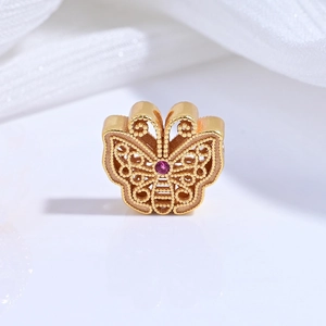 Macro shot of gold-plated butterfly bead with filigree details and a red gemstone