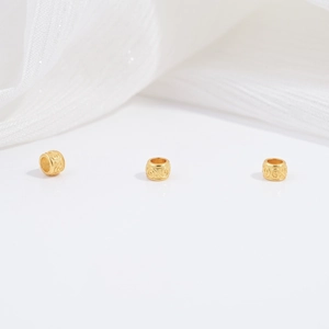 Close-up of three gold-plated silver cylindrical beads with vintage scroll engravings