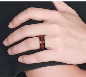 Dettaglio anello 8mm in acciaio nero con intarsio in venature di legno rosso sulla mano uomo