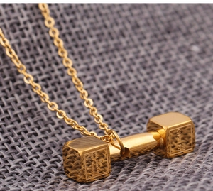 Macro detail of golden dumbbell necklace with 'Believe you can' motivational engraving