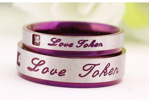 Gros plan de bagues de couple en acier brossé avec intérieur violet et texte Love Token gravé
