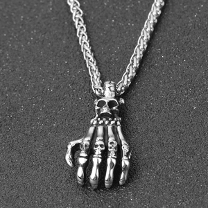 Macro shot of punk skeleton hand pendant with detailed skulls and thick wheat chain