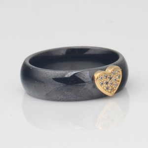 Detail of 6mm black ceramic ring with gold heart-shaped zircon inlay on a grey surface