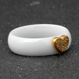 Detail of a white ceramic ring featuring a gold heart shape inlaid with zircon crystals
