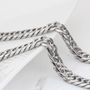 Macro shot of 4mm stainless steel cuban link chain resting on a white embossed ceramic plate