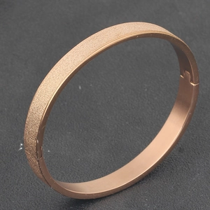 Close-up of rose gold stainless steel bangle featuring matte finish and hinged closure