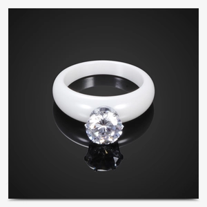Primer plano de un anillo de cerámica blanca con circón grande sobre fondo negro reflectante