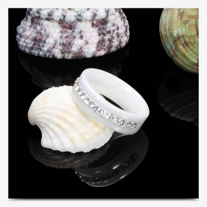 Macro detail of white ceramic ring with single row of cubic zirconia on a seashell