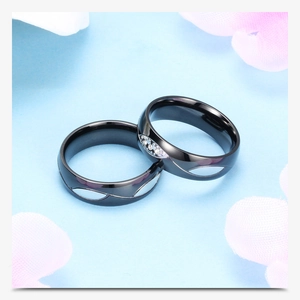 Detalle de anillos de pareja negros de acero con diseño calado ondulado y cristal incrustado