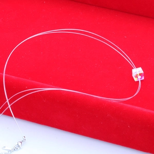 Minimalist fishing line necklace with rainbow crystal cube pendant on red velvet stand