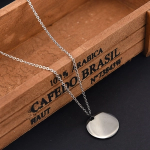 Close-up of a 25mm round stainless steel pendant necklace on a rustic wood box