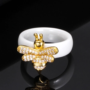 Anillo de cerámica blanca de 6mm con abeja dorada y cristales pavé sobre fondo de espejo negro