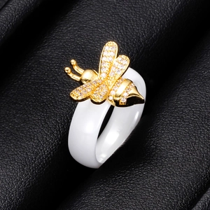 Detalle macro de anillo de cerámica blanca con motivo de abeja dorada y circonitas