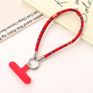 Detailed view of red ethnic woven phone strap with silver metal ring and fixing pad