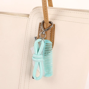 Mint green acetate comb keychain with faux leather bow charm on a beige tote bag handle