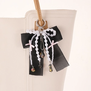 Detail of elegant black ribbon bow bag charm with pearl tassels and pink accent