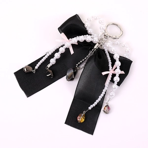Detail of black satin bow charm with white pearls and pink ribbon on white background