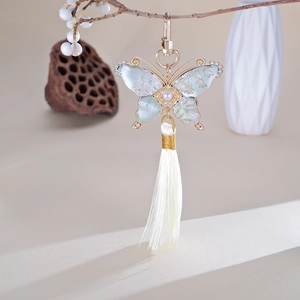 Détail du charm papillon en soie brodée avec strass et pompon en soie blanche