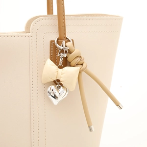 Llavero elegante de cuero crema con lazo y colgante de corazón en un bolso blanco