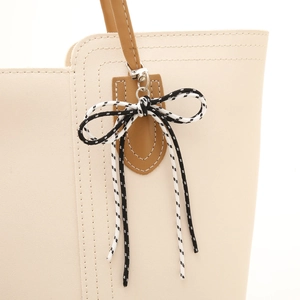 Cream tote bag with brown straps featuring a black and white checkered bow charm