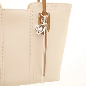 Chic beige leather tote bag with heart charm and tassel detail on brown handles