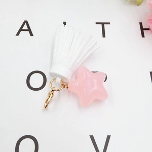 Close-up of pink star charm with white faux leather tassel on a golden lobster clasp