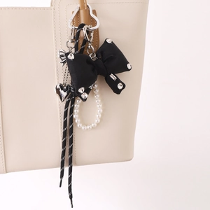 Stylish rhinestone bow bag charm with pearls and woven nylon cord on a beige handbag