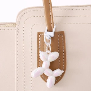 Iridescent white acrylic balloon dog charm on a beige leather bag with a silver metal ring