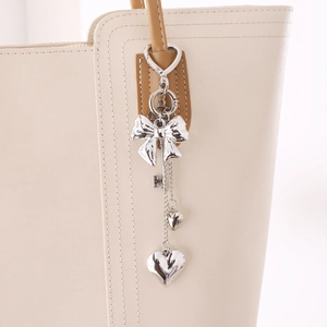 Silver Y2K metal bow keychain with heart pendants on a cream leather tote bag