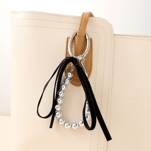 Silver bead keychain with black ribbon bow hanging on an elegant beige leather bag