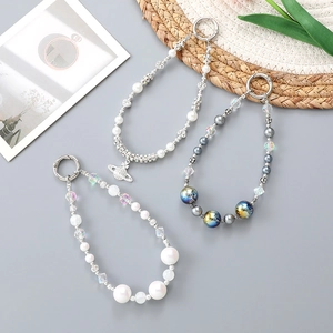 Handmade beaded phone charms with pearl beads and saturn planet pendants on gray surface