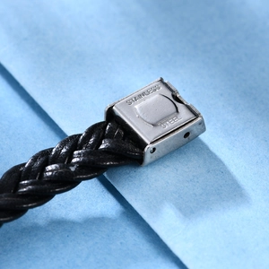 Detalle de una pulsera de cuero trenzado negro con cierre cuadrado de acero inoxidable mate