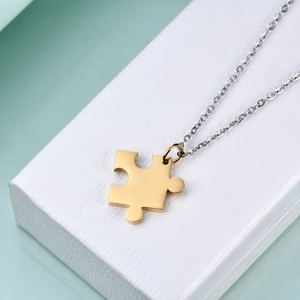 Detail of a gold puzzle piece pendant paired with a slim silver chain on a white display box