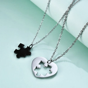 Close-up of matching puzzle piece and heart cut-out necklaces for couples in polished metal