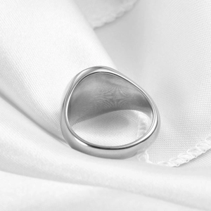 Polished silver signet ring displayed on white satin fabric with mirror-like metallic finish