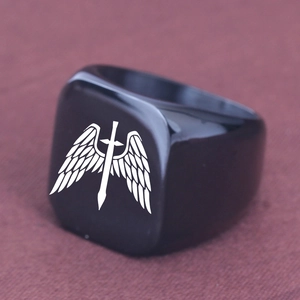 Dettaglio macro di un anello a sigillo nero opaco con motivo laser di ali e spada bianca