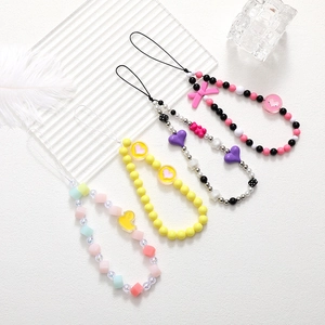 Detail of four colorful beaded phone straps with bow, heart, and bear charms on white background