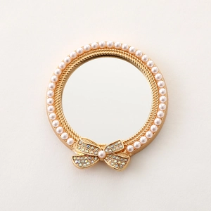 Detailed view of a gold compact mirror with white pearls and a rhinestone-encrusted bow